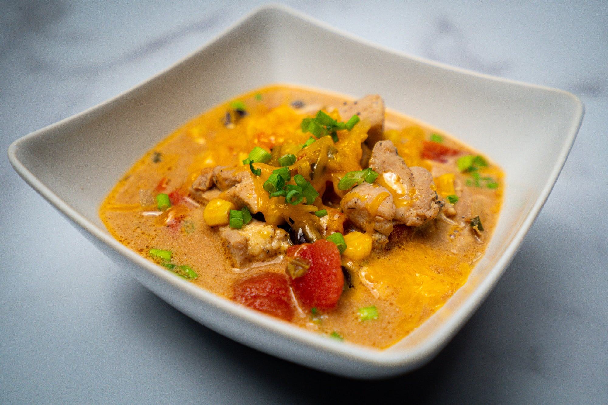 Taco soup in white bowl with Chicken, green onion and tomatoes in broth